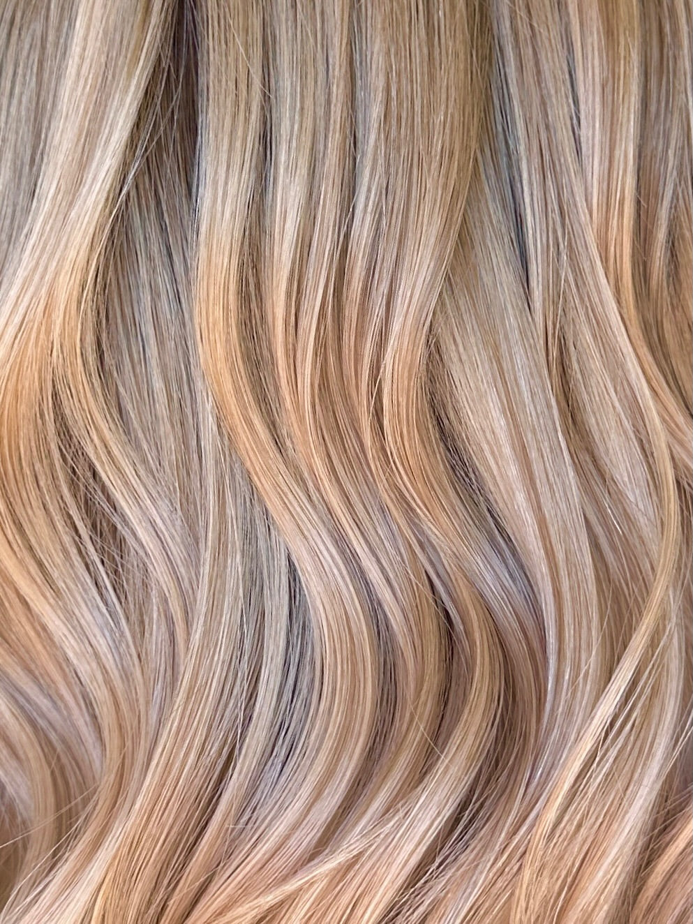 Highlighted golden blonde hair extensions showing various shades of blonde and brown with smooth wavy texture.