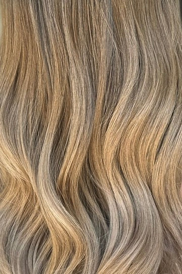 Close-up image of wavy dark blonde wig showing the ombre effect with a blend of neutral and cool tones.