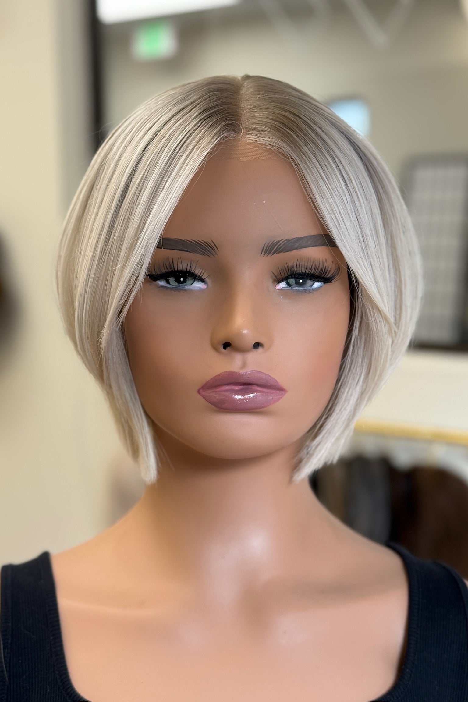 A mannequin head displaying a bright blonde wig with a short, straight cut and a part in the middle.