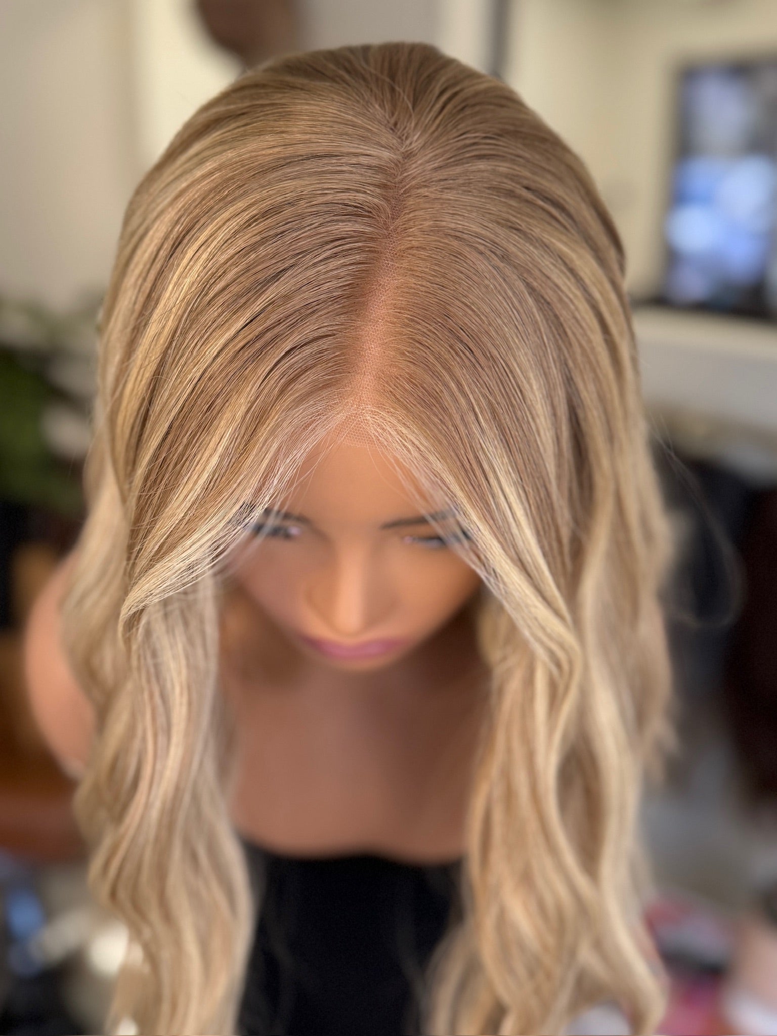 Blonde wig with wavy hair style on a blurred background, showing part line on wig for women with hair loss, chemo patients