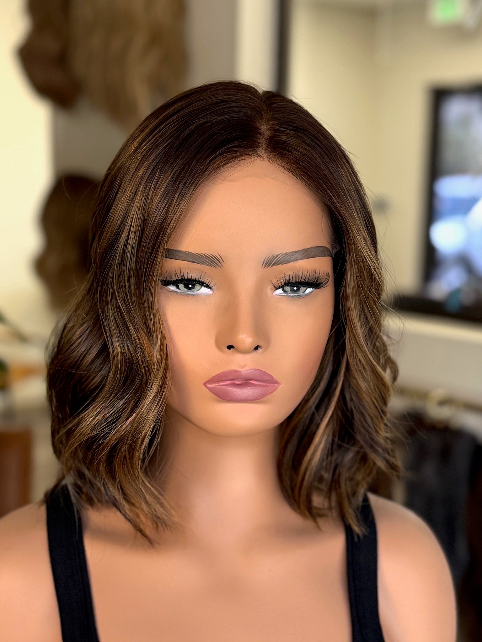 Mannequin head with brown wavy hair in a blurred indoor setting